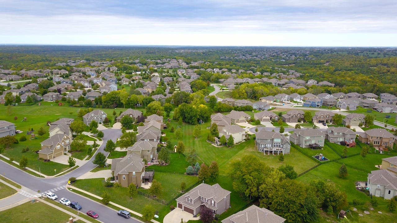 About-01 aerial view of a suburban neighborhood with houses, roads, and lush greenery.