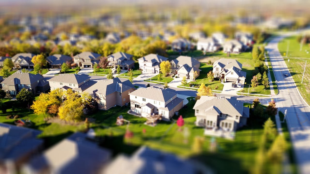 About-02 tilt-shift aerial photo of a suburban neighborhood with green lawns and roads.