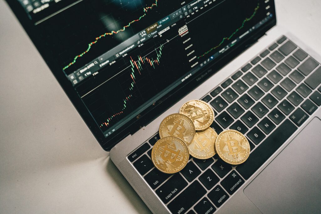 Golden Bitcoin Coins Placed On A Laptop Keyboard With Trading Chart Displayed On The Screen.