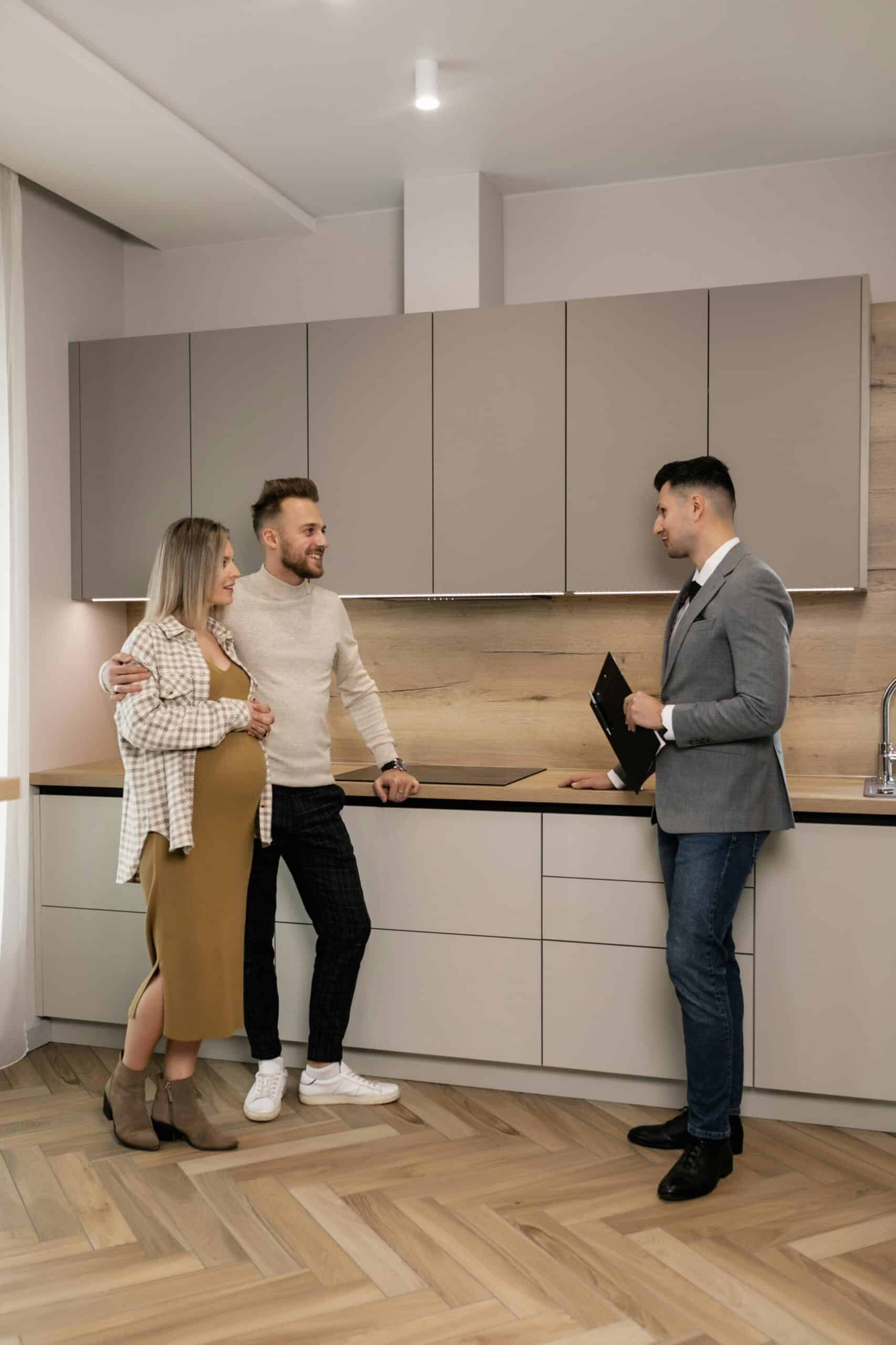 Pregnant Couple Joyfully Discussing Their Future Home Purchase With A Real Estate Agent In A Modern Kitchen.